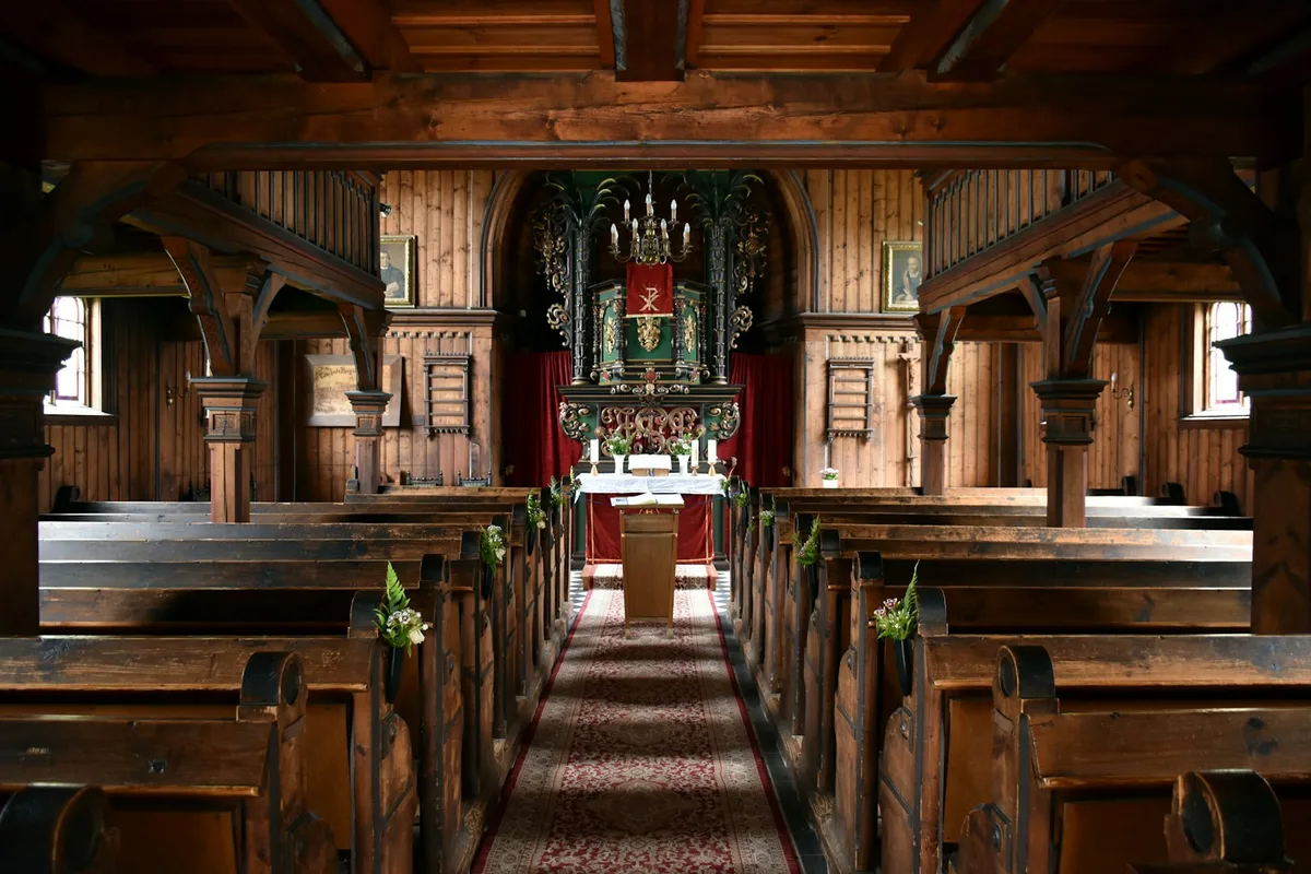 Interior de uma bela igreja vazia com bancos de madeira organizados em direção ao altar iluminado.