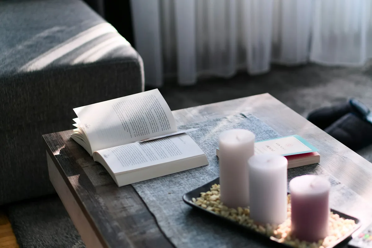 Uma vela acesa ao lado de um livro aberto sobre uma mesa de madeira.